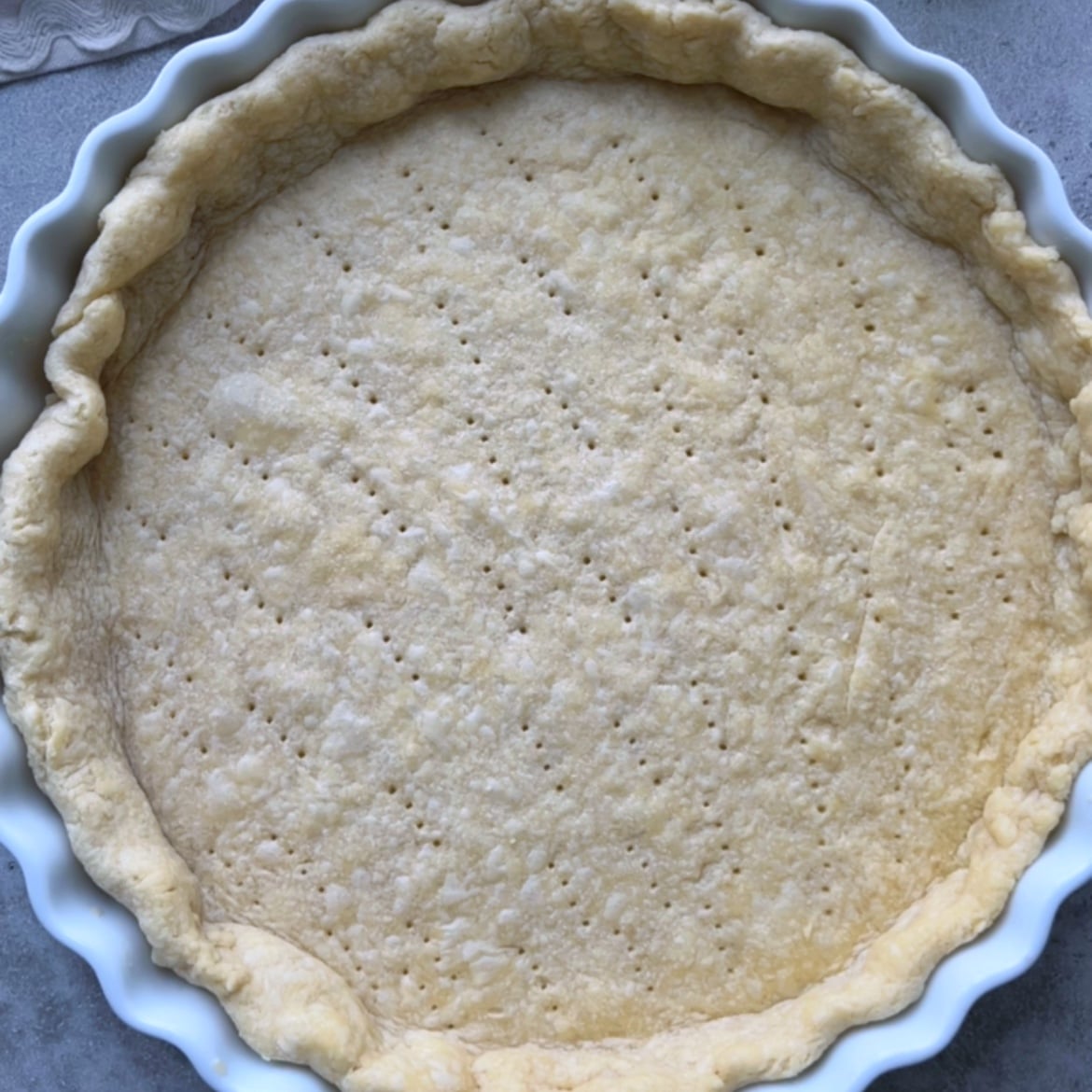 Unbaked pie crust in a white ceramic dish, with fork marks evenly pricked across the bottom.