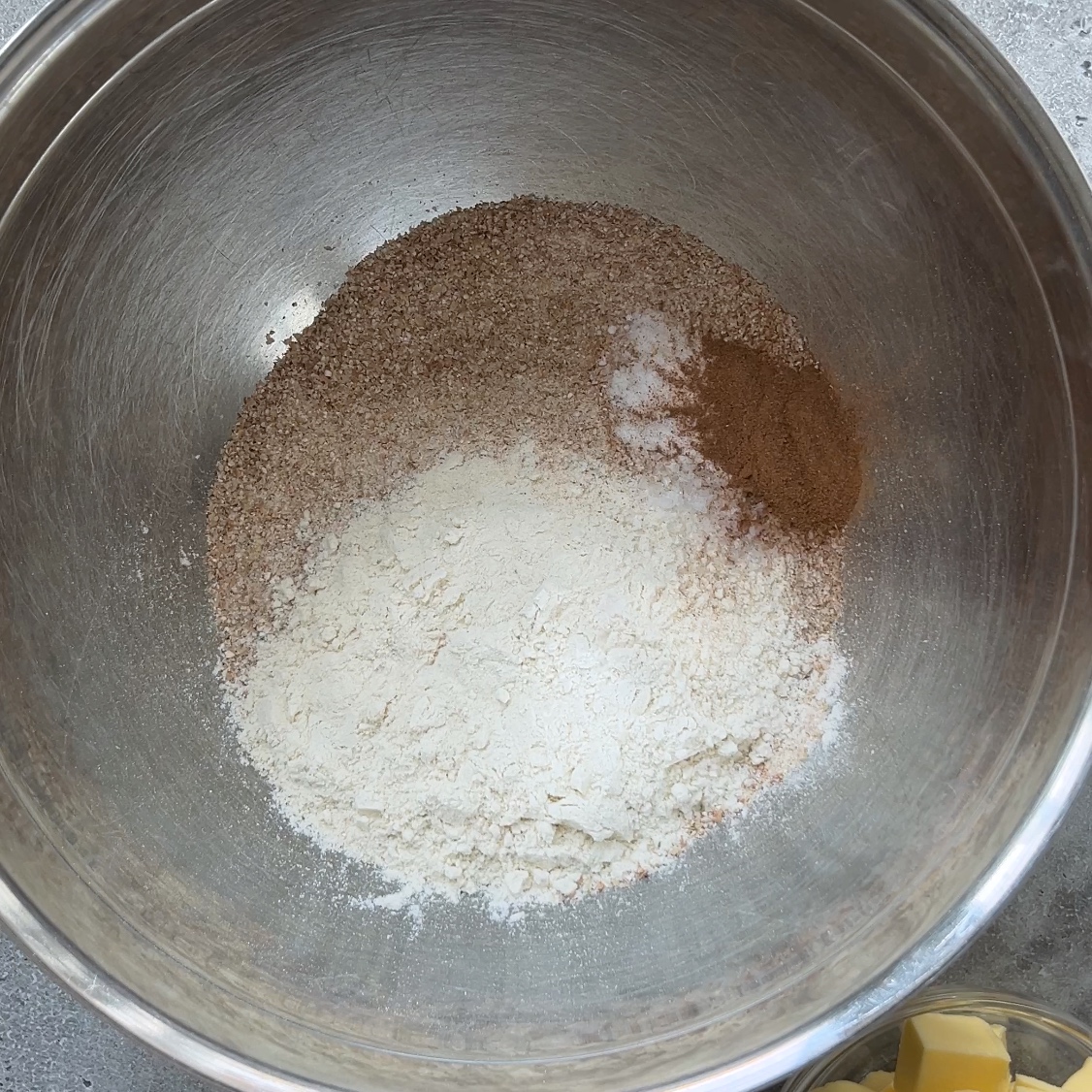 A metal mixing bowl containing graham flour, white flour, sugar, baking soda, salt, and cinnamon.