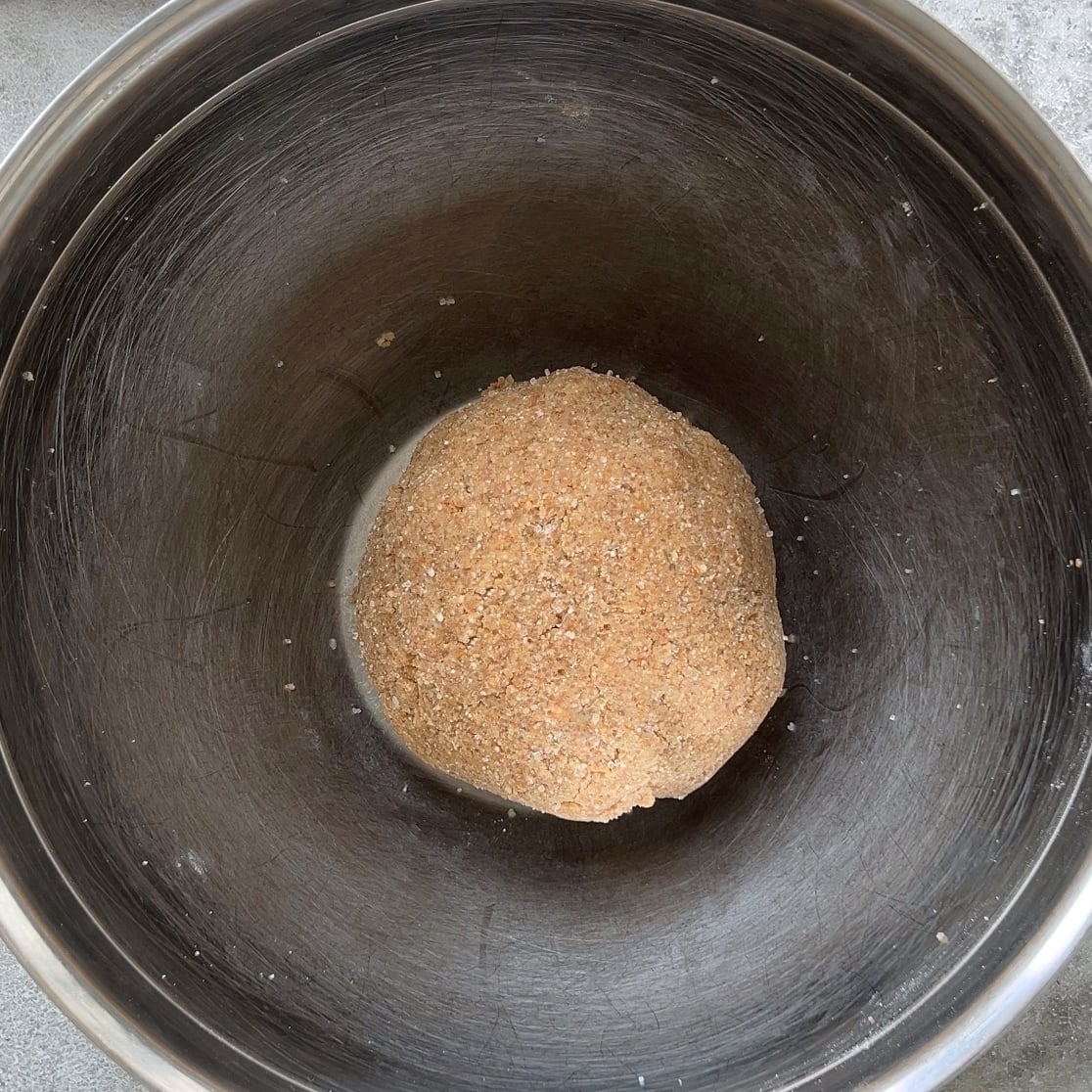 A ball of brown dough in the center of a large metal mixing bowl.