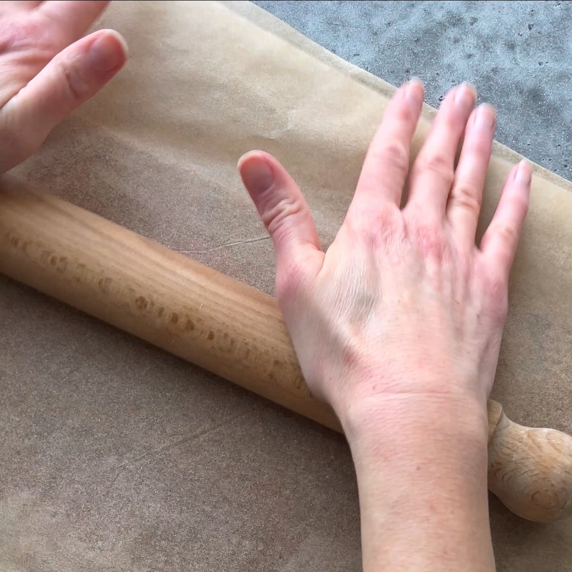 Two hands flatten graham cracker dough between two layers of parchment paper with a rolling pin.