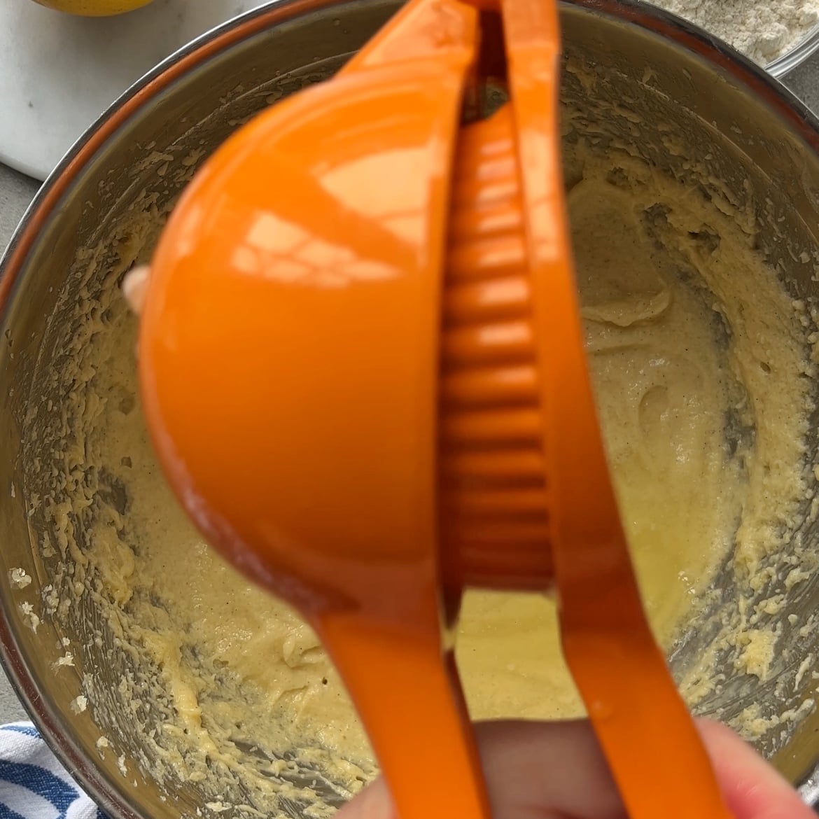 A hand holding an orange citrus squeezer over a mixing bowl containing yellow batter.