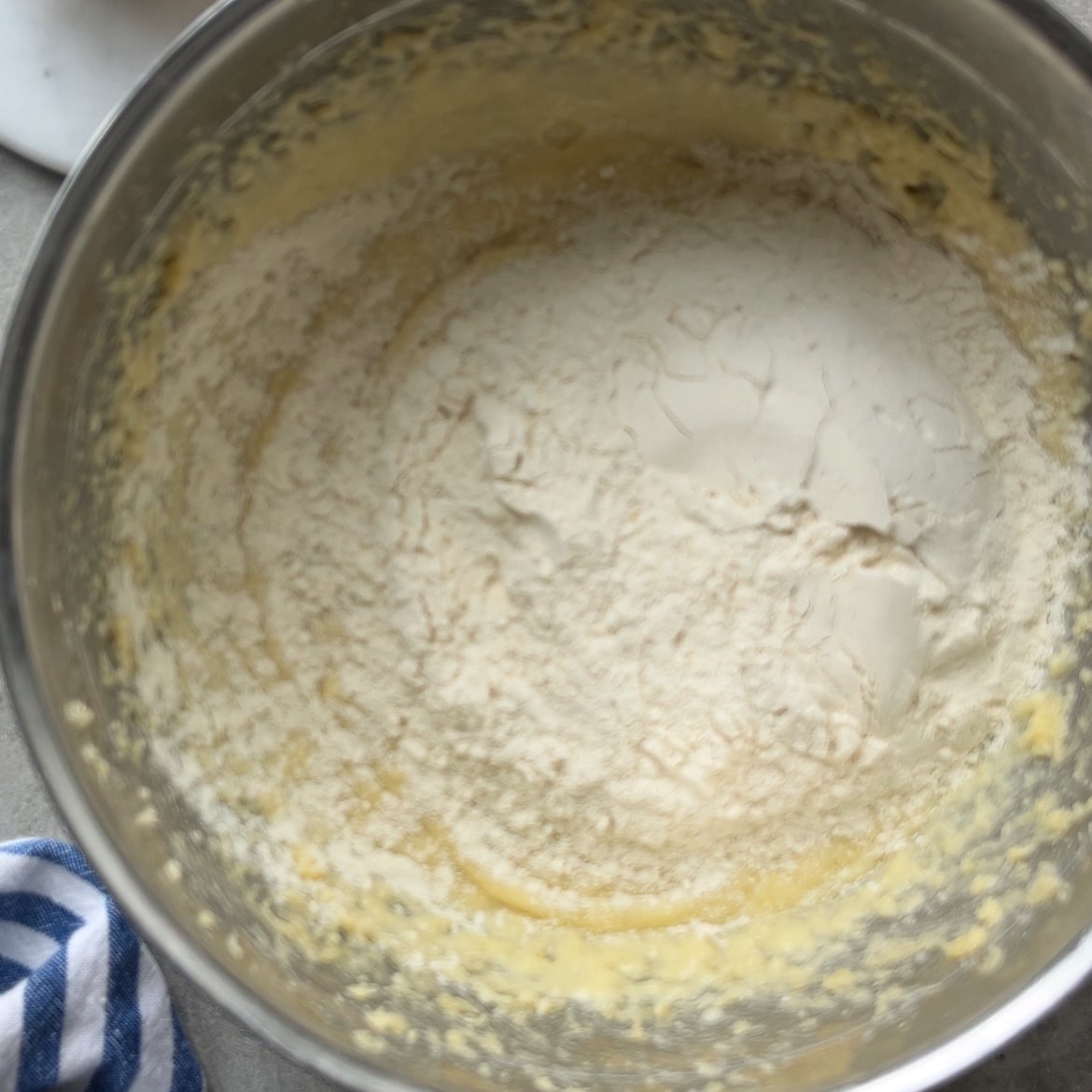 A metal mixing bowl containing flour and wet ingredients being mixed for a lemon cake.