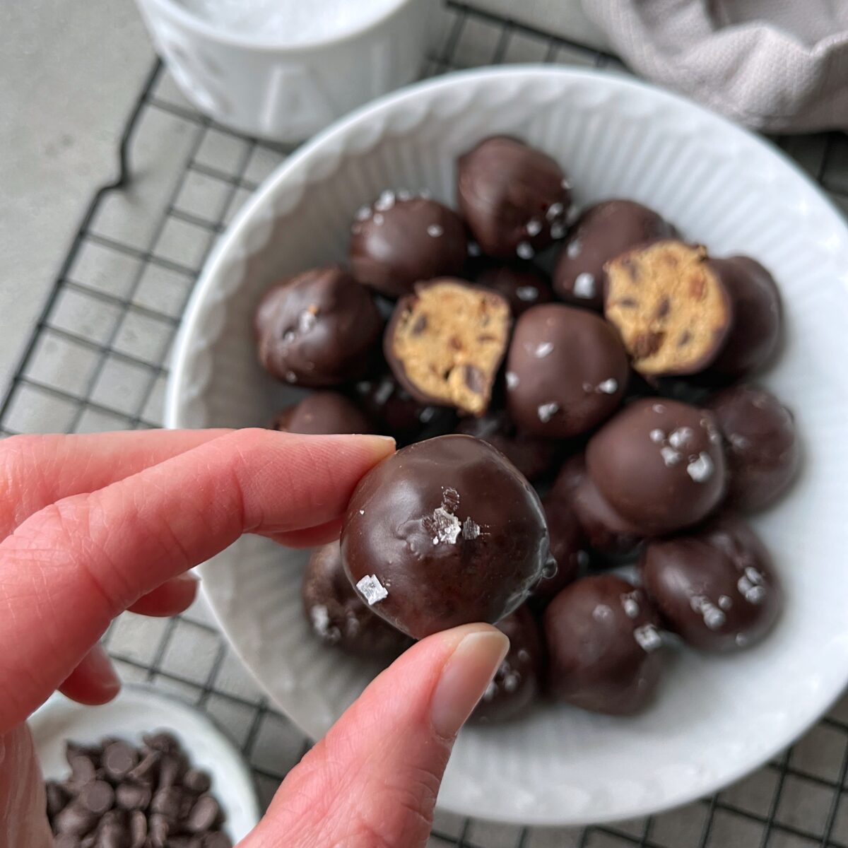 A hand holds a chocolate-covered cookie dough bite topped with sea salt.