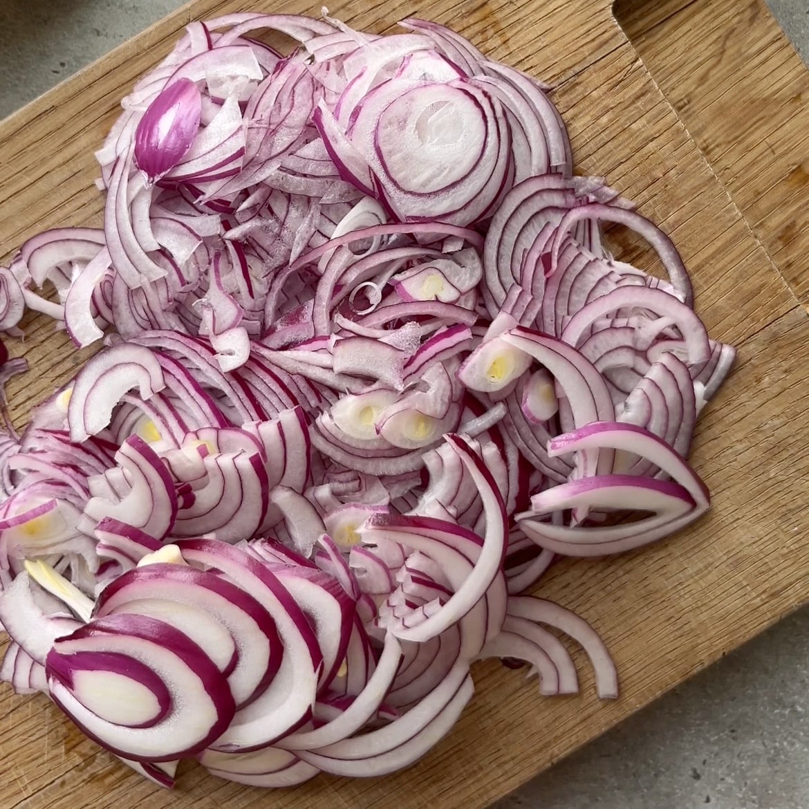 Thinly sliced red onions on a wooden cutting board,.