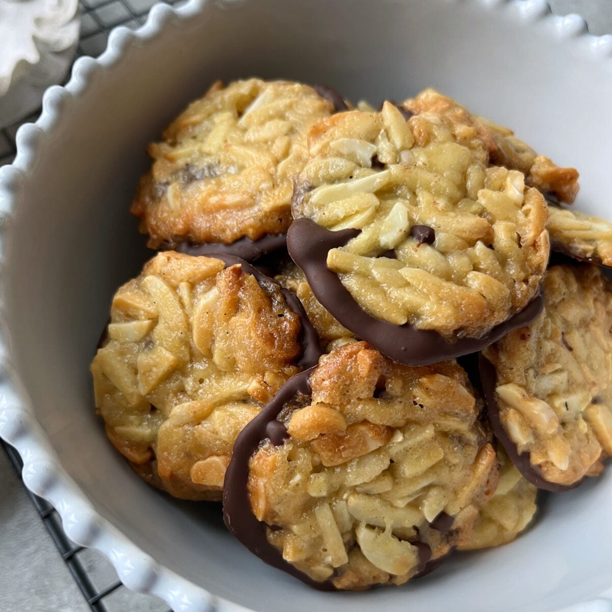A bowl of Florentines dipped in chocolate, arranged closely together in a white scalloped bowl.