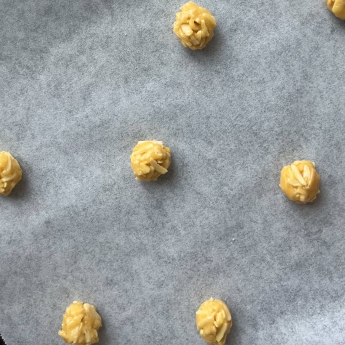 Balls of raw Florentine cookie dough spaced out on a parchment-lined baking tray, ready to be baked.