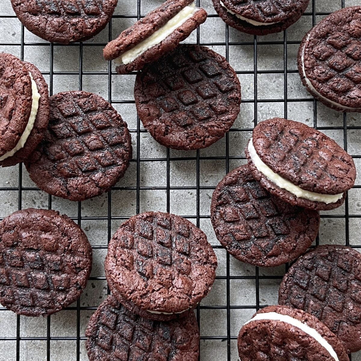Homemade Oreos with cream filling are arranged on a wire cooling rack.