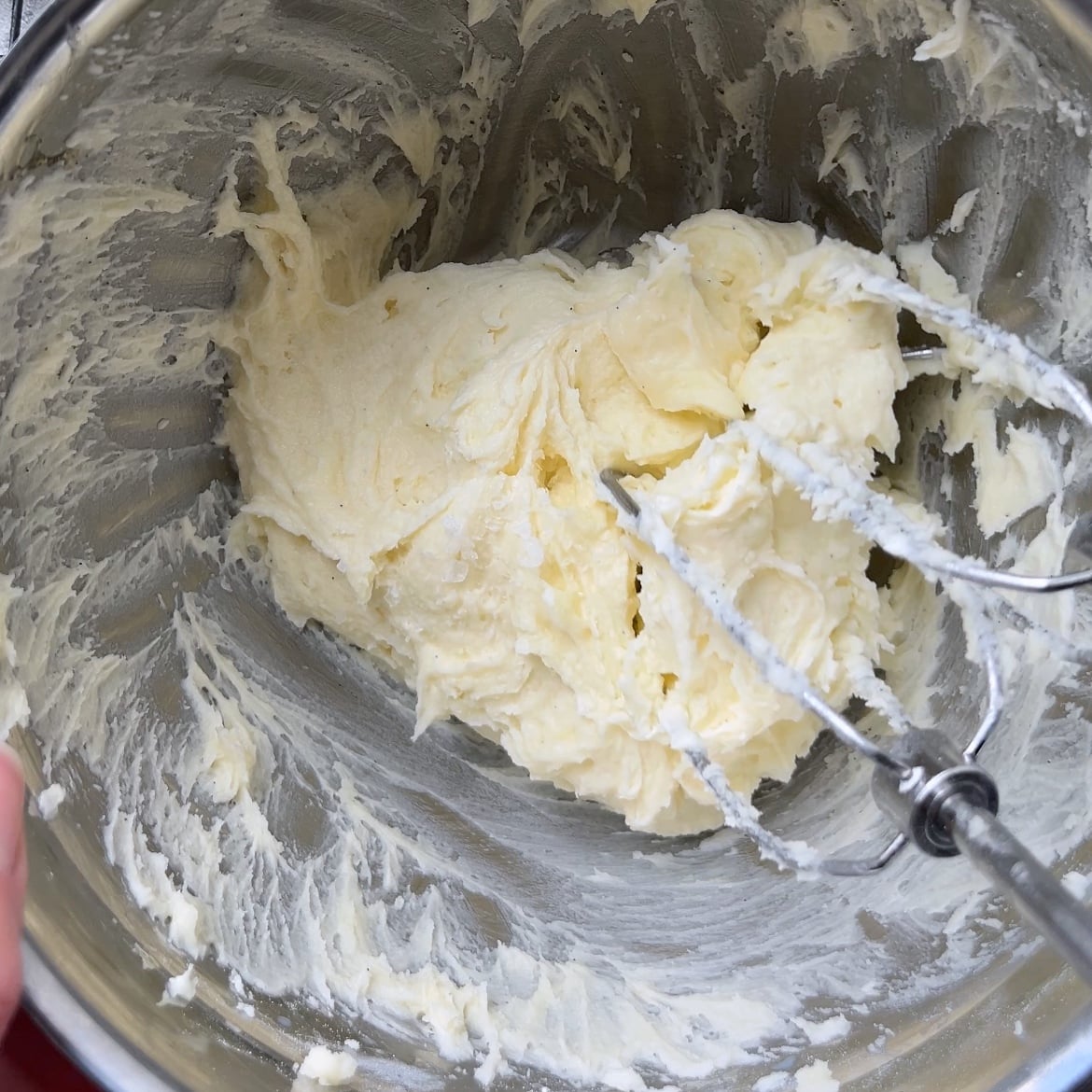 Electric beaters mixing creamed butter and powdered sugar in a metal bowl.