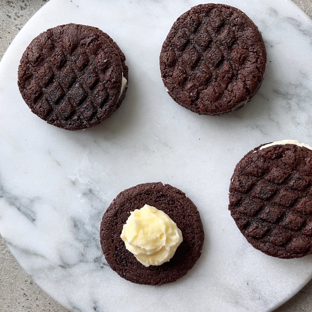 Three Oreo Cookies, three assembled and one open-faced with a dollop of cream filling, are arranged on a round marble surface.