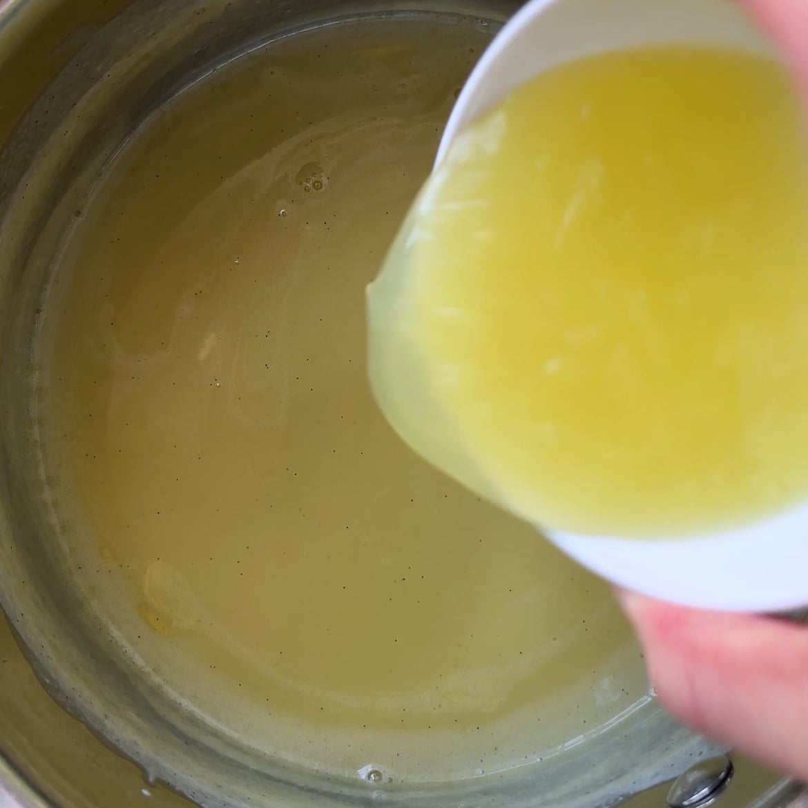 A hand pours lemon juice into a pot containing a creamy mixture.