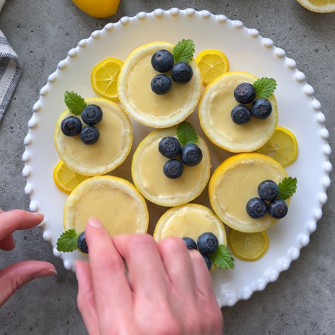 A hand tops a blueberry onto a lemon posset.