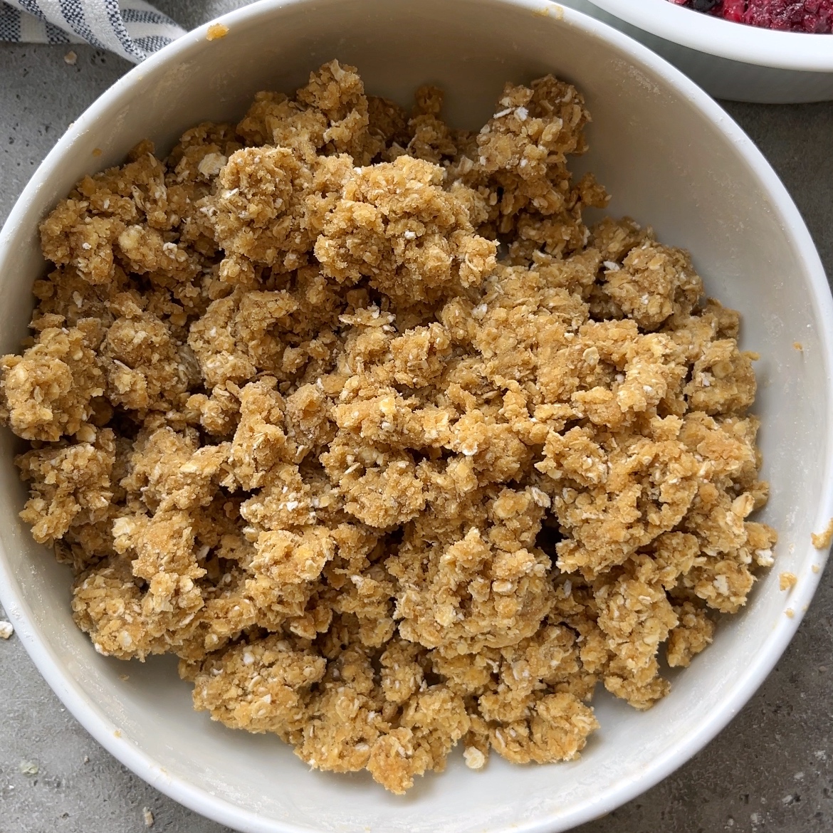Bowl filled with crumbly oat, flour, butter, and brown sugar mixture.