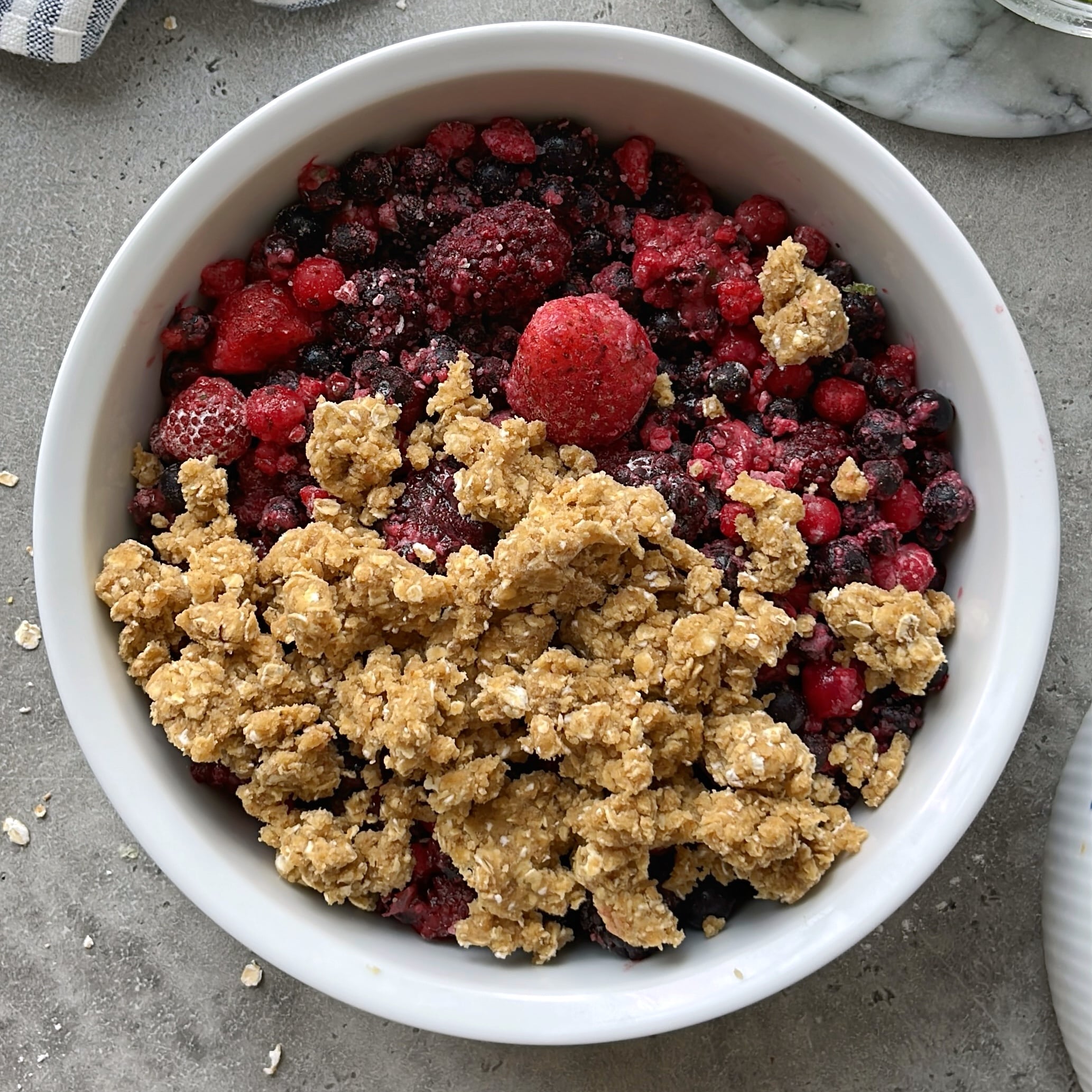 A white bowl filled with a delicious mixed berry medley, topped with an oat and crumb mixture, ready to be baked.