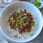 A bowl of white rice topped with savory Mongolian Ground Beef, sliced green onions, and sesame seeds.