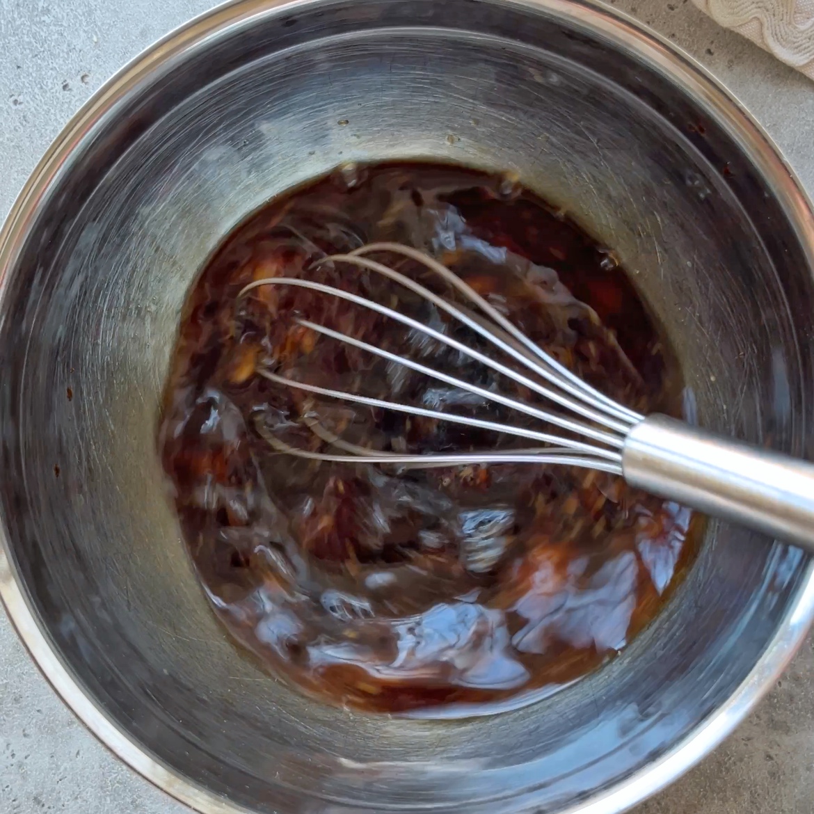 A metal whisk stirs a dark Mongolian Ground Beef sauce in a stainless steel mixing bowl.