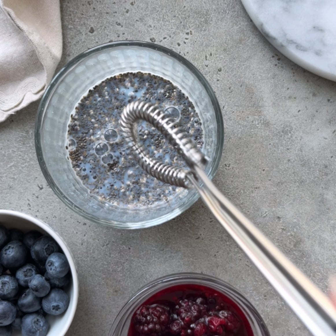 A glass with chia seeds soaking in milk is being whisked. 