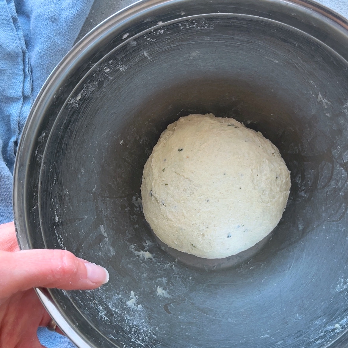 A hand holds a metal bowl containing a ball of dough, ready to be transformed into artisan crackers.
