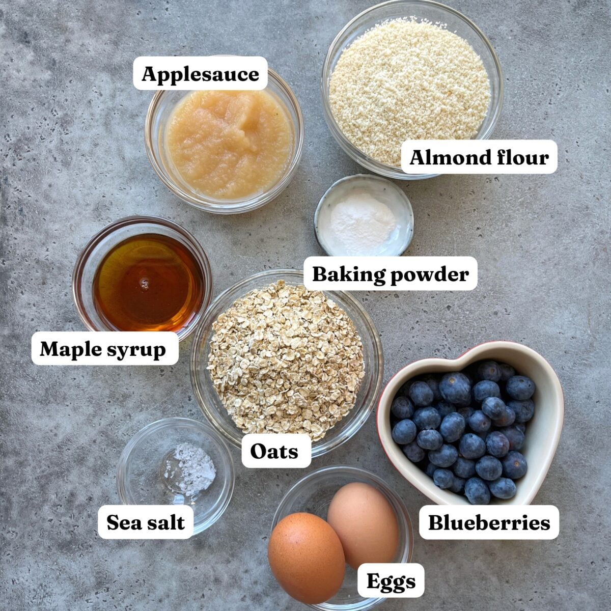 Top-down view of applesauce, almond flour, baking powder, maple syrup, oats, blueberries, sea salt, and two eggs.