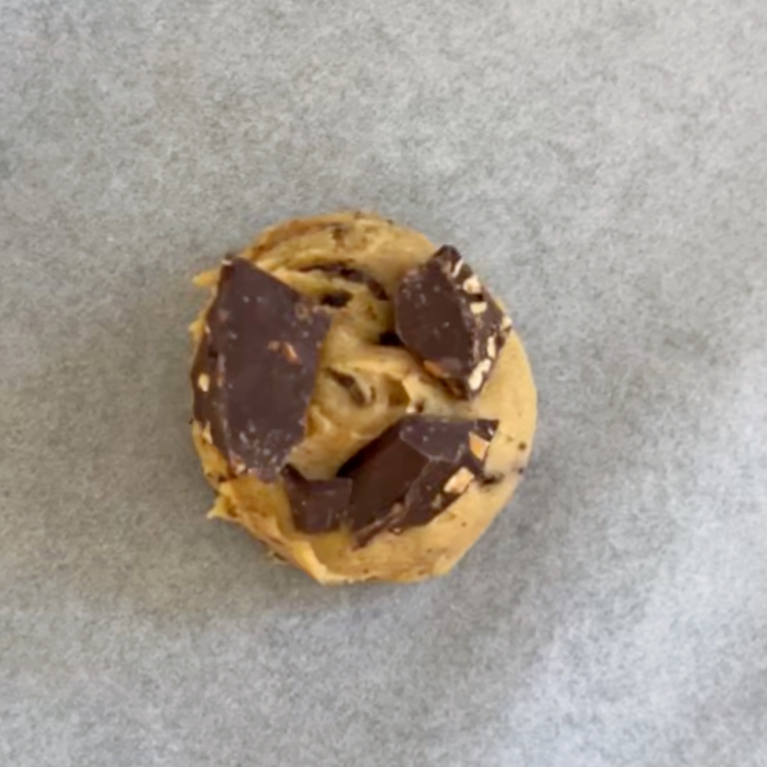 A ball of chewy chocolate chip cookie dough with large chocolate chunks sits on a sheet of parchment paper ready to bake.