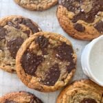 Chewy Chocolate Chip Cookies with large melted chocolate pieces and a sprinkling of sea salt are arranged on parchment paper next to a small white bowl of coarse salt.