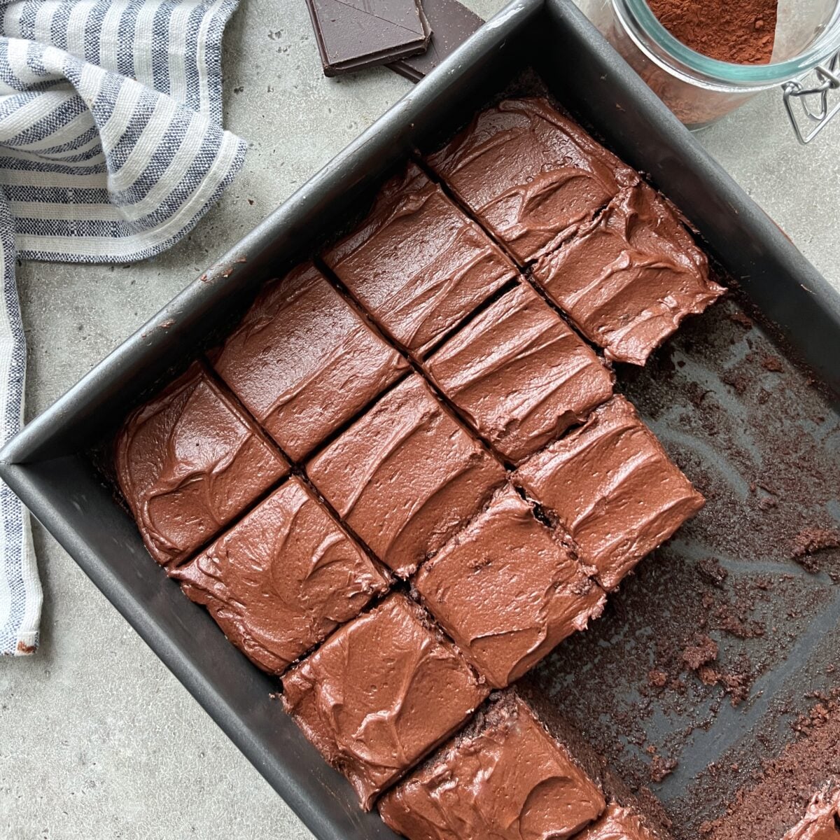 A rectangular baking sheet pan filled with evenly cut, chocolate-frosted cake.