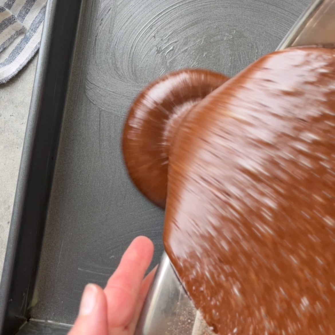 Batter is being poured from a bowl into a greased rectangular baking pan.