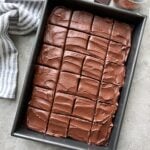 A rectangular baking pan filled with a chocolate cake topped with chocolate frosting and cut into even squares.