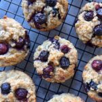 Baked blueberry treats cool on a black wire rack, viewed from above on a gray surface.