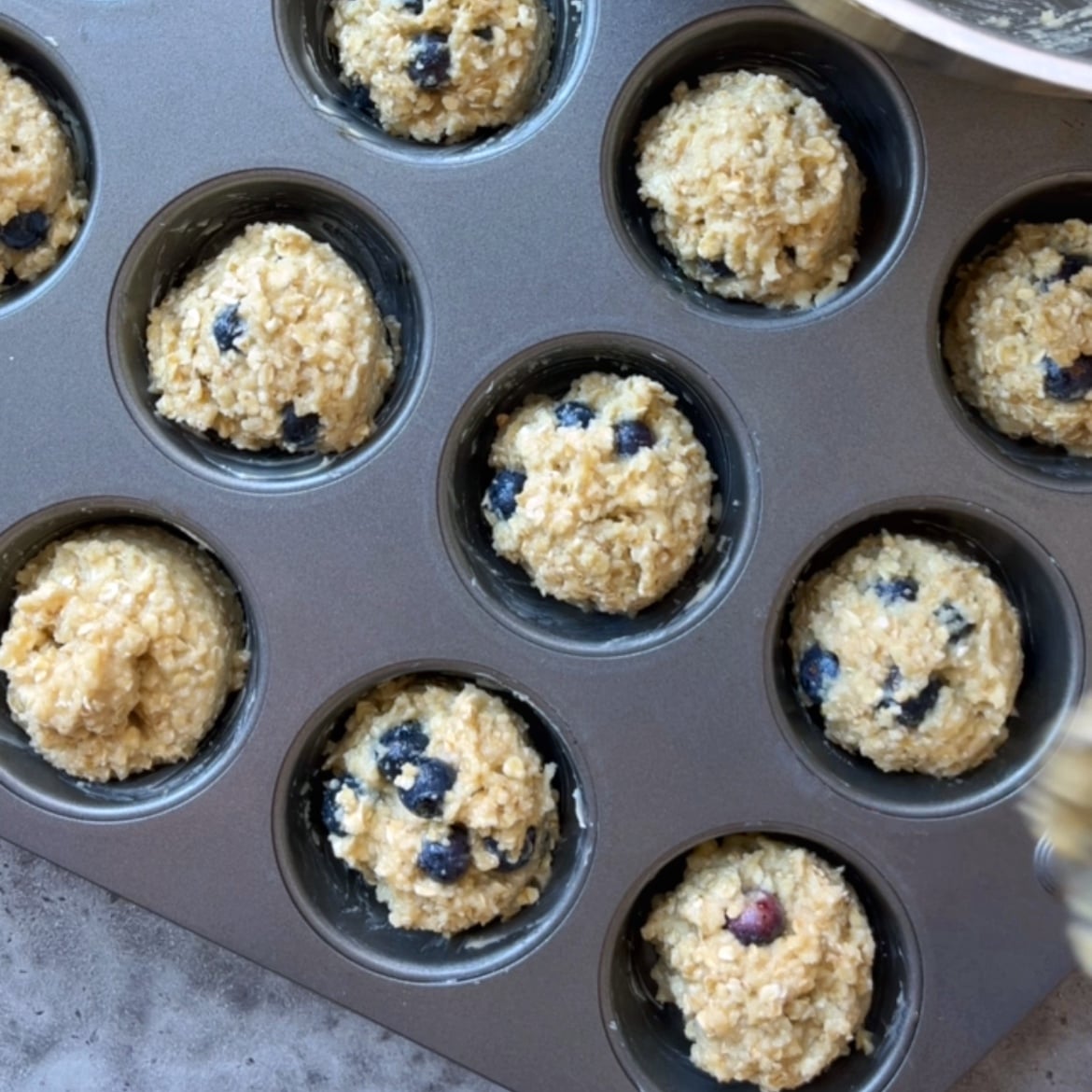 Muffin tin filled with unbaked oats and blueberry muffin batter.