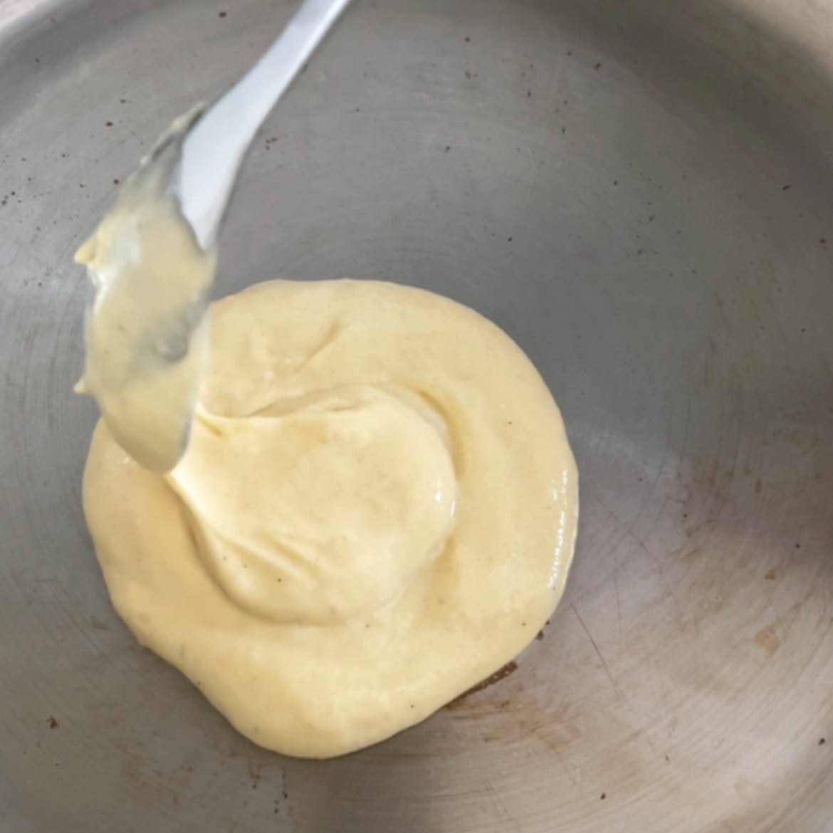 A spoon drops thick yellow batter onto a round metal pan.