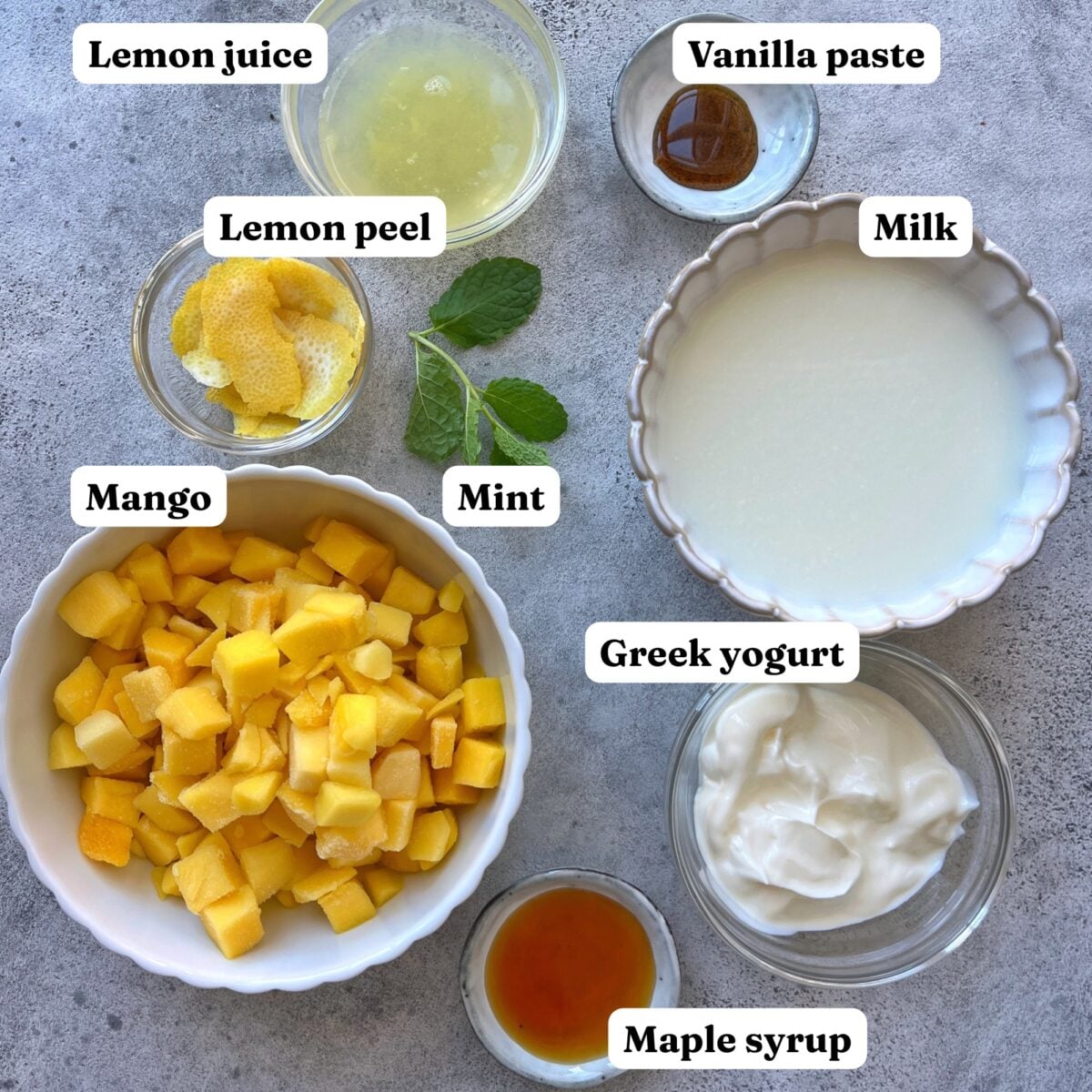 Bowls containing diced frozen mango, lemon juice, lemon peel, mint, vanilla paste, milk, Greek yogurt, and maple syrup.