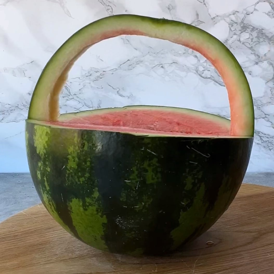 A watermelon basket with the top cut off and a handle carved from the rind sits on a wooden surface.