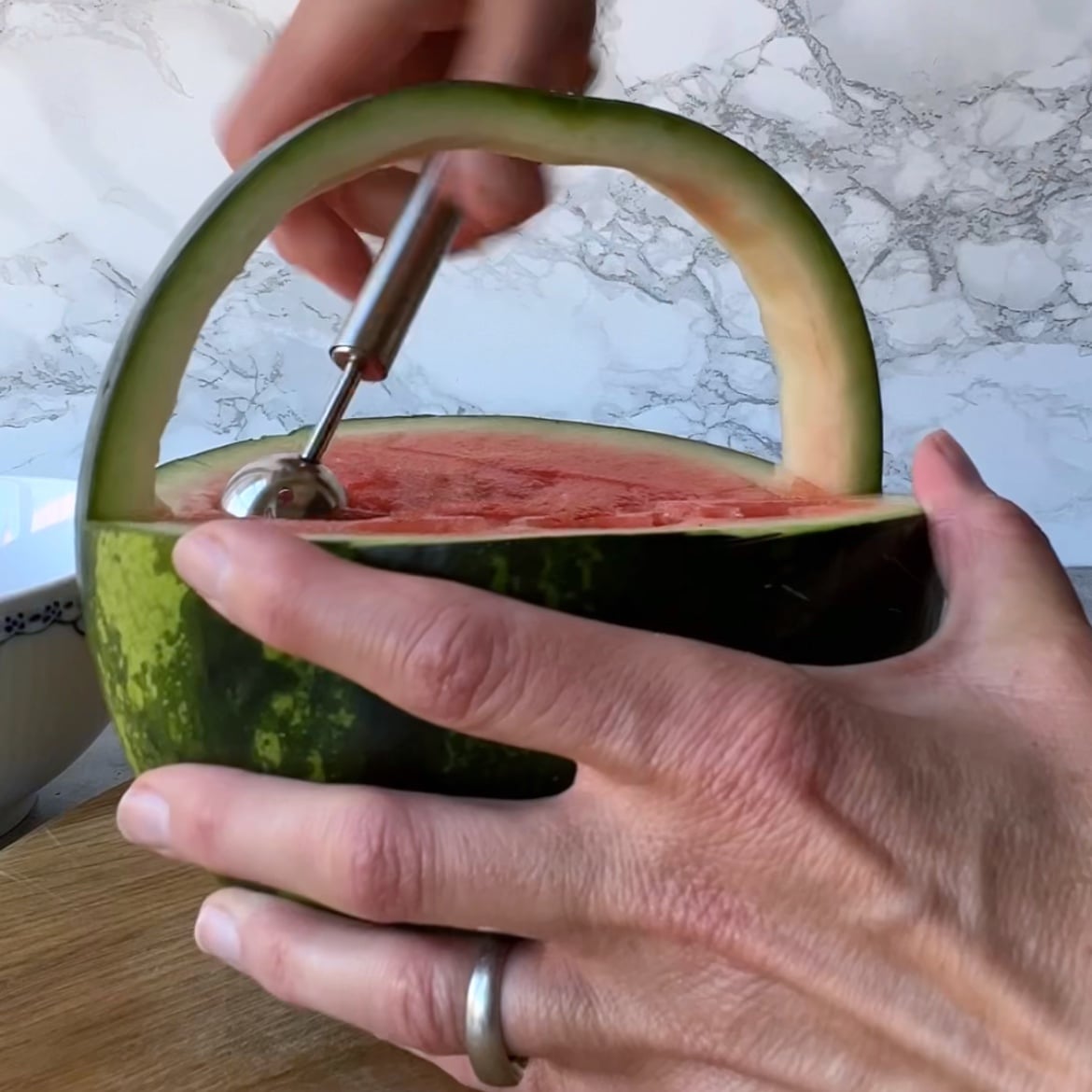 A person uses a melon baller to scoop out juicy watermelon from a Watermelon Basket.