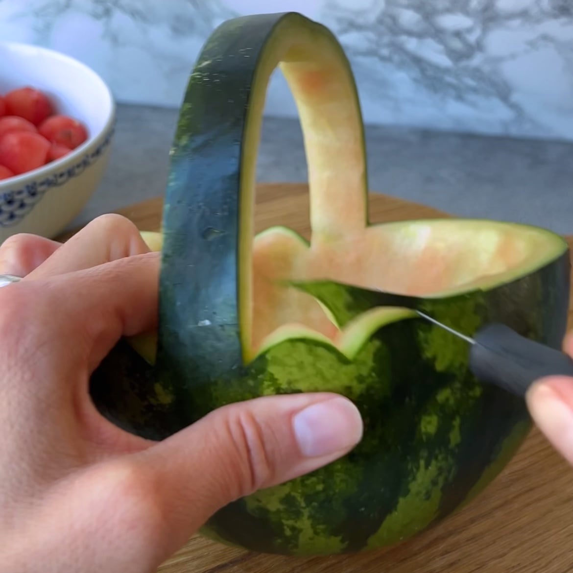 A person carves a scalloped edge on a watermelon basket.