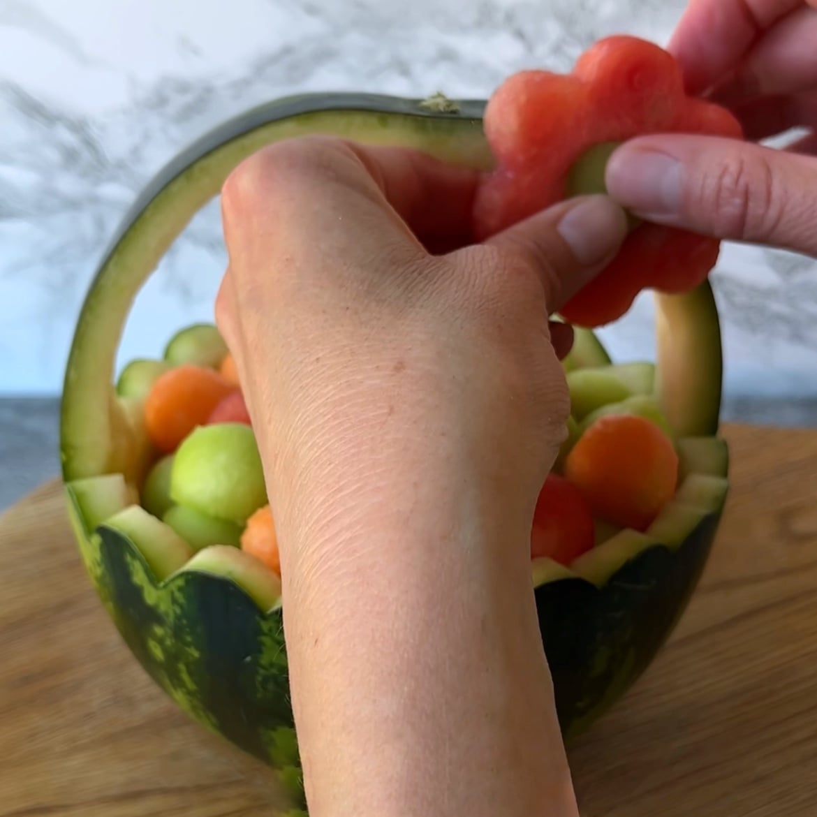 A hand places a flower-shaped watermelon slice into a charming Watermelon Basket.