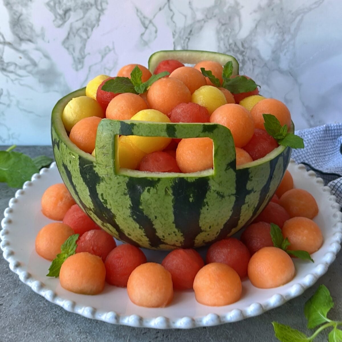 Watermelon basket with two handles filled with mango, watermelon, and cantaloupe balls.