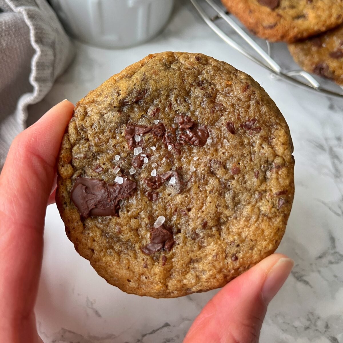 A hand holds a banana bread cookie topped with coarse sea salt.