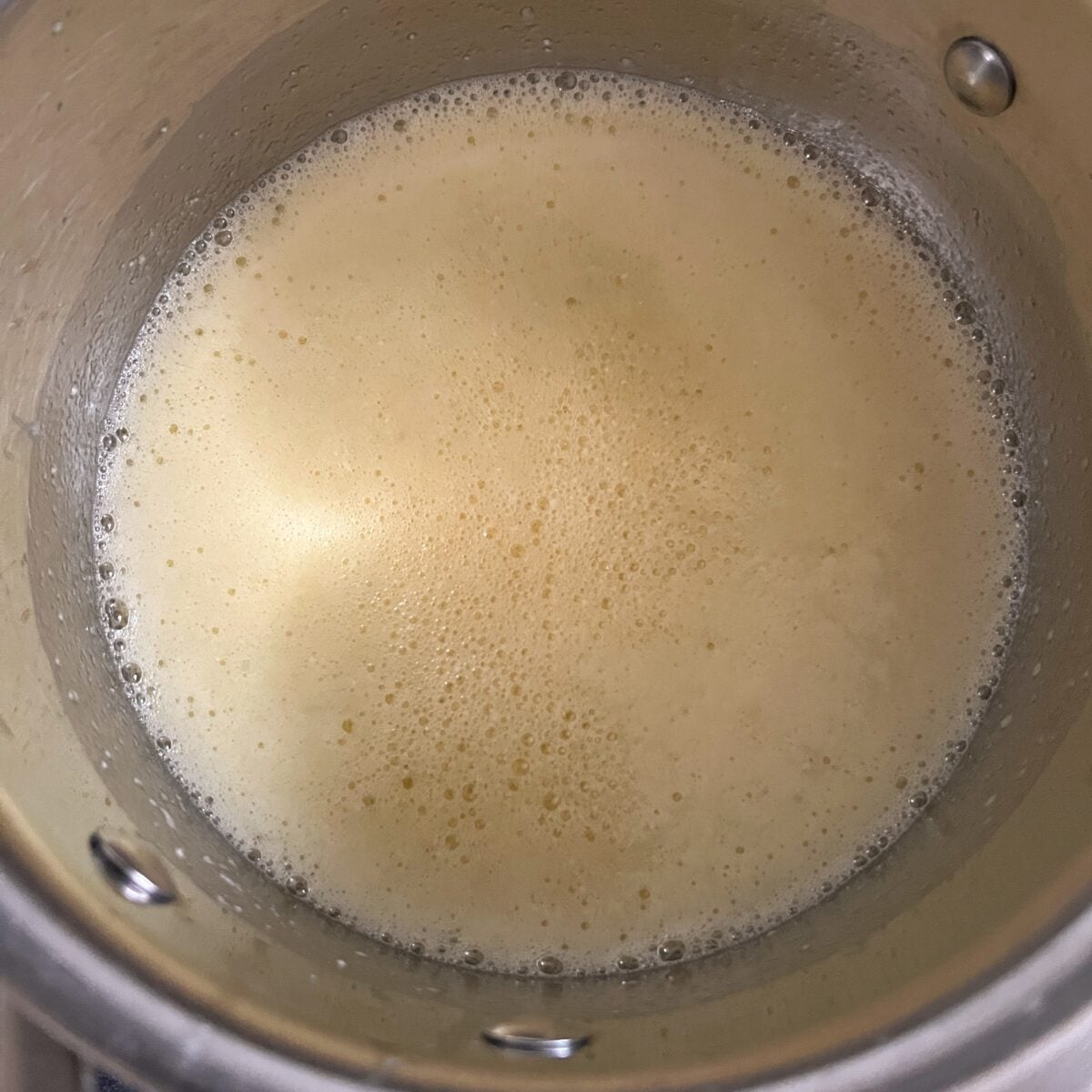 A close-up of a metal pot containing foamy butter.