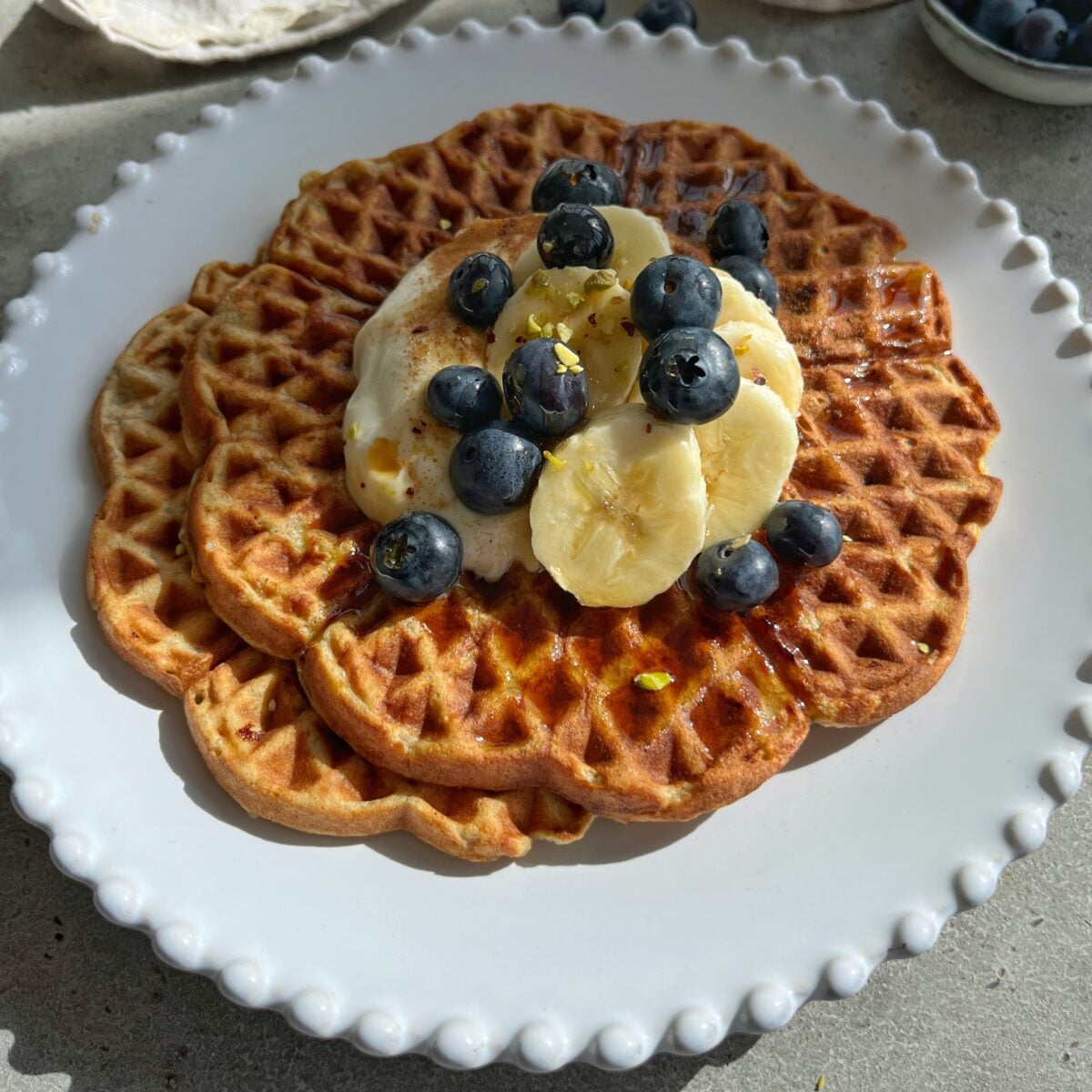 Two waffles topped with banana slices, blueberries, and a dollop of Greek yogurt and maple syrup are served on a white plate.