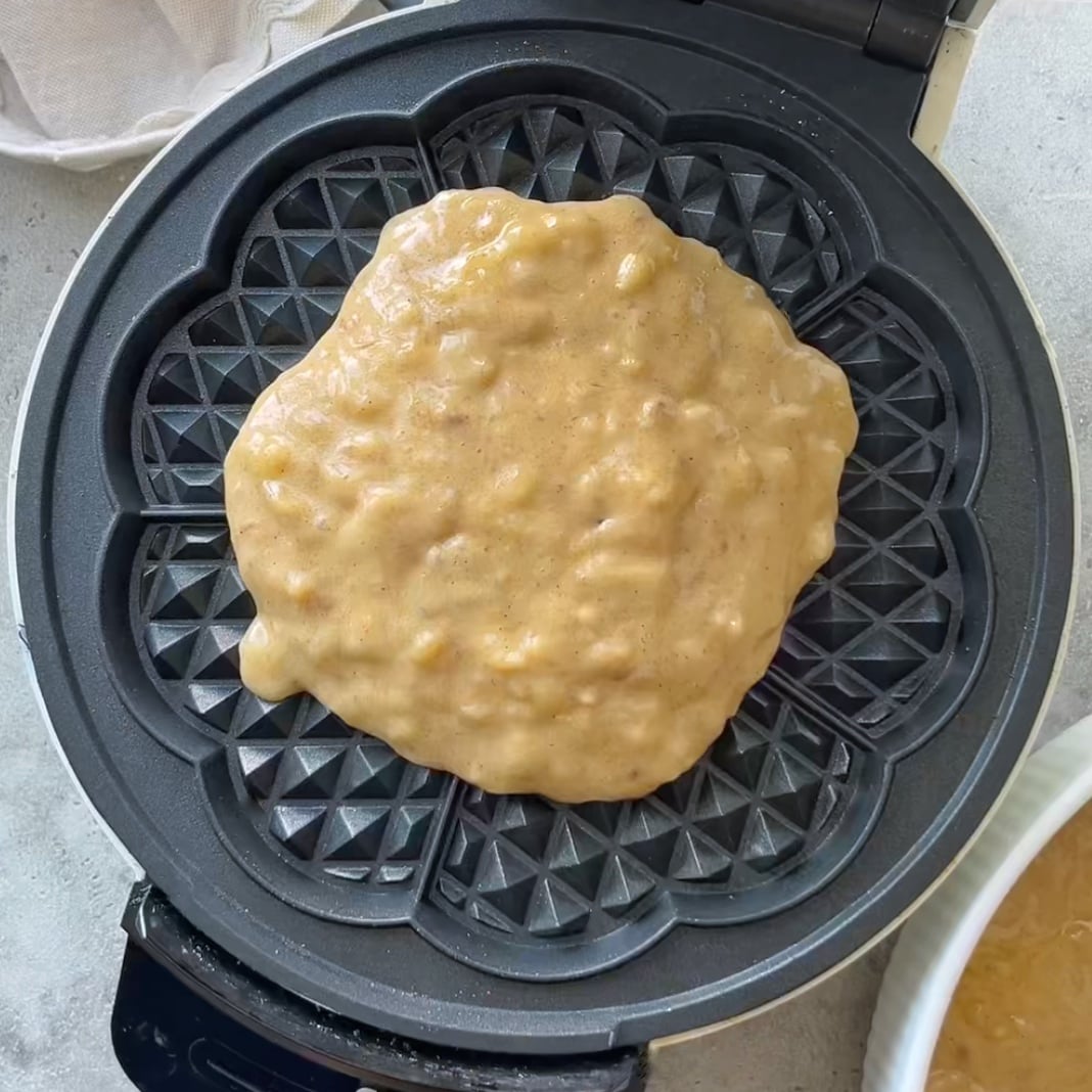 A waffle iron topped with batter is ready to be baked into banana waffles.