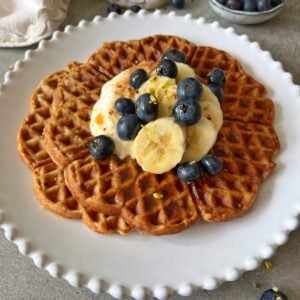 Two waffles topped with banana slices, blueberries, Greek yogurt, and a sprinkle of chopped nuts on a white plate.
