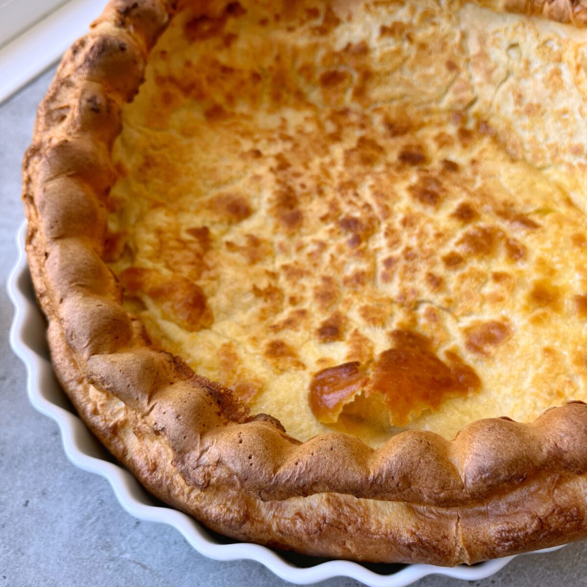A close-up of a baked German Pancake with a puffy golden-brown crust in a white ceramic dish.