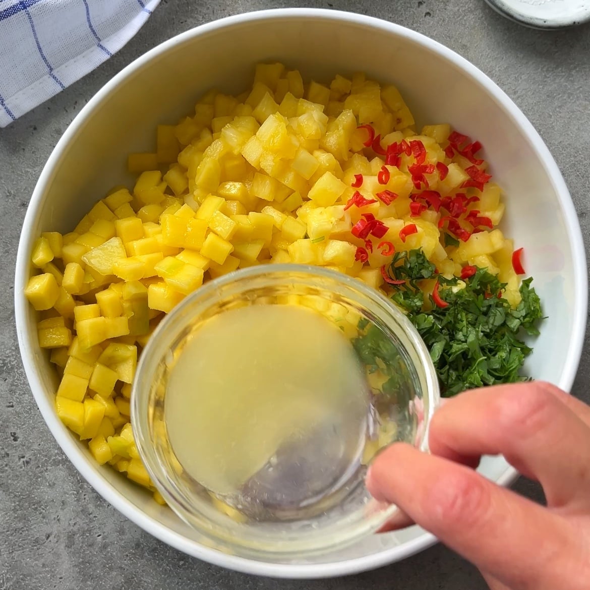  A hand is pouring lime juice into a bowl containing pineapple salsa.