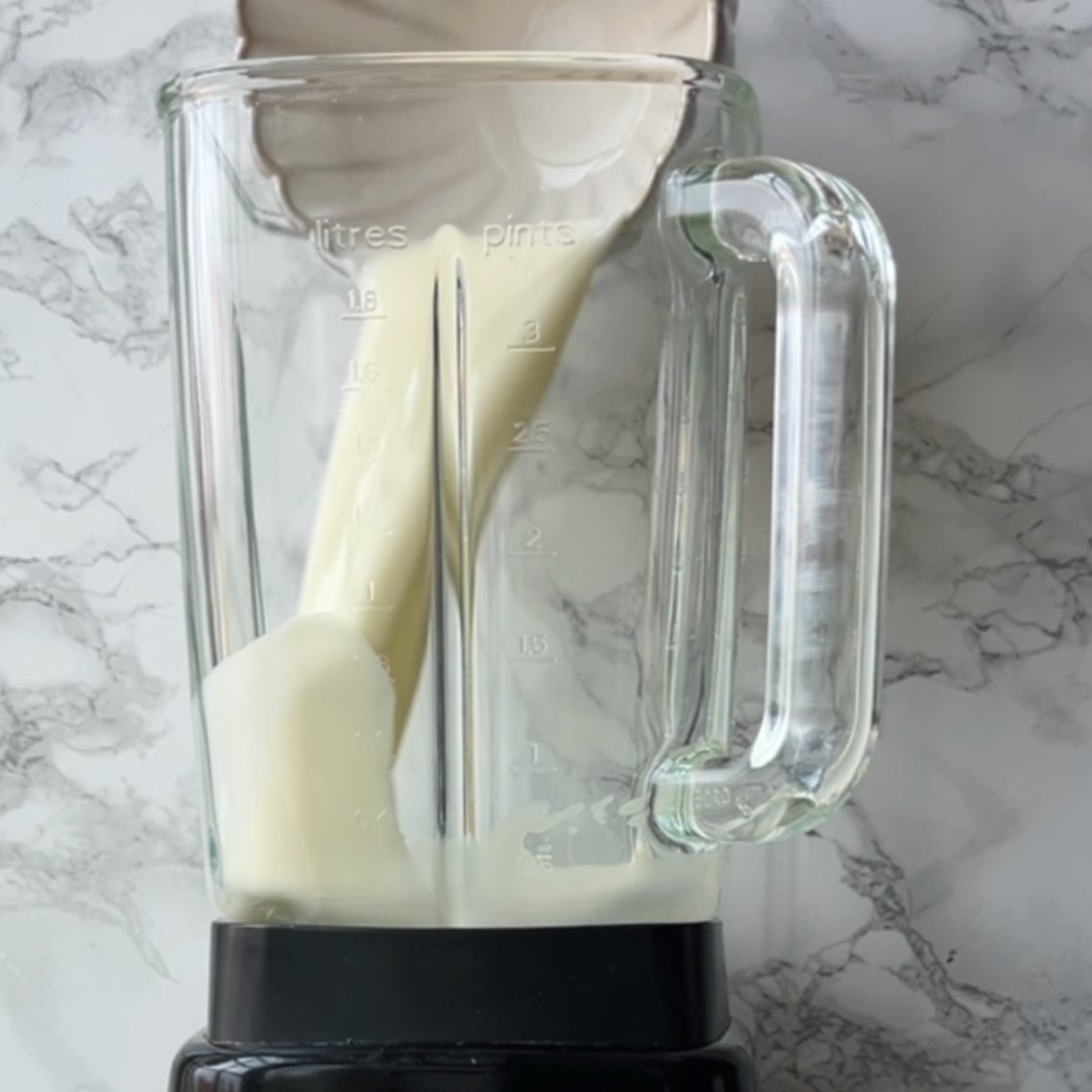 Milk being poured from a jug into a glass blender jar, ready to create a refreshing pineapple smoothie.