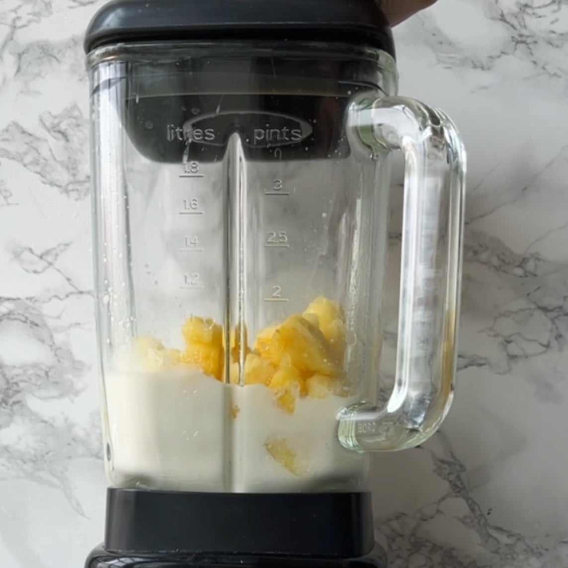 A blender with milk and pineapple chunks inside ready to blend into a refreshing pineapple smoothie.