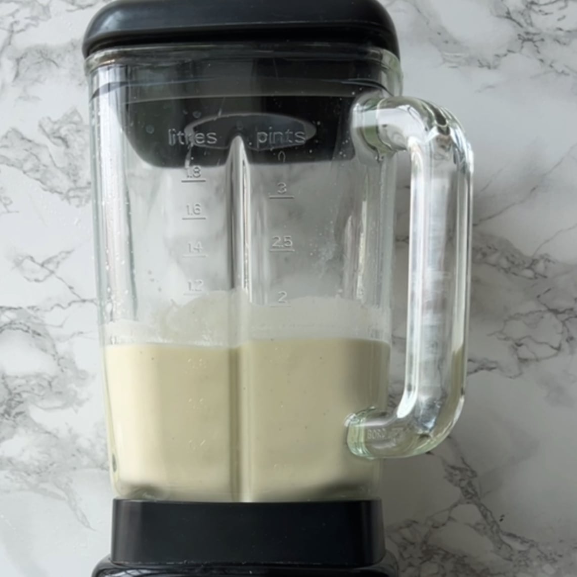A blender filled with a light-colored pineapple smoothie.
