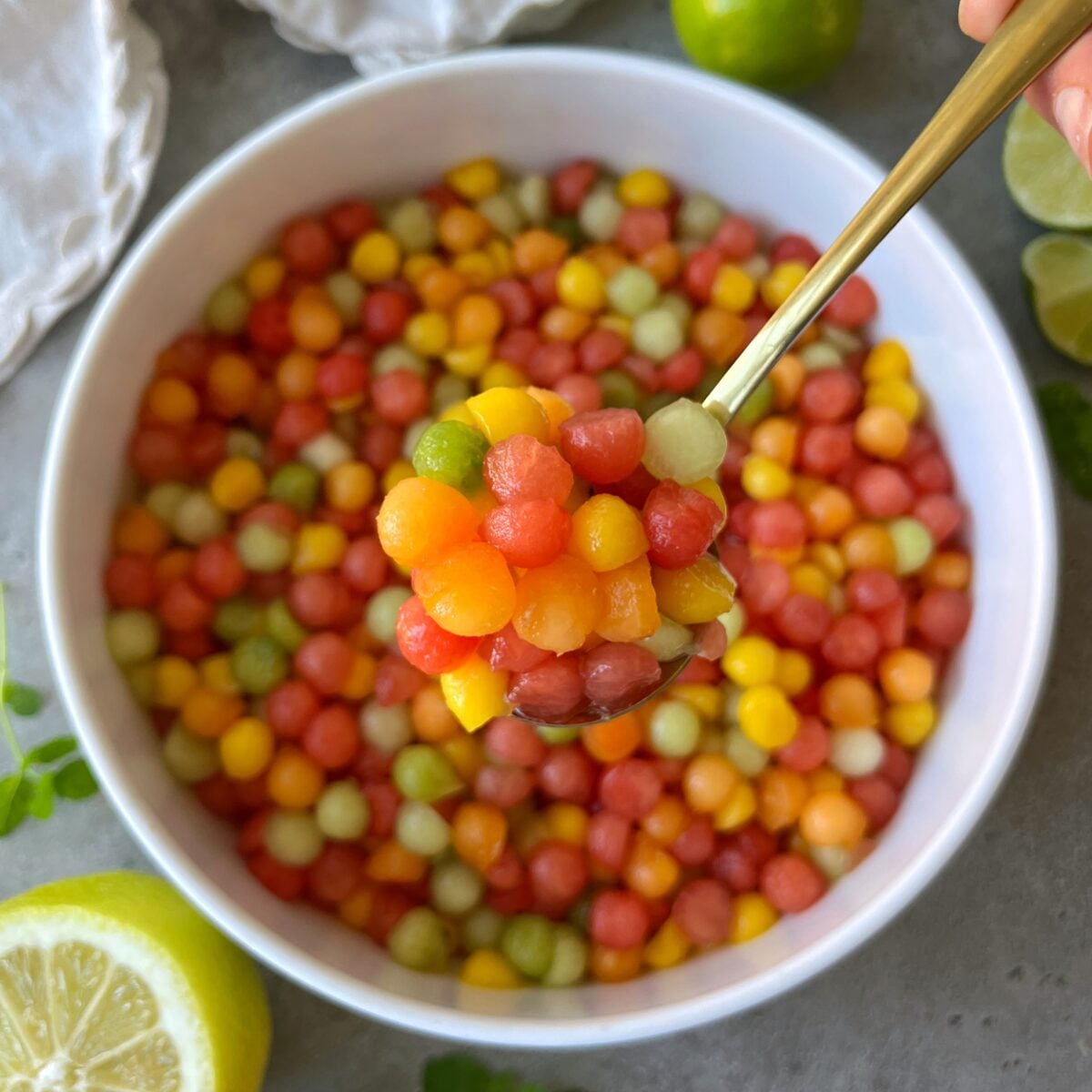 A closeup of a spoon topped with fruit balls including mango, kiwi, Gallia melon, watermelon, and apricot.