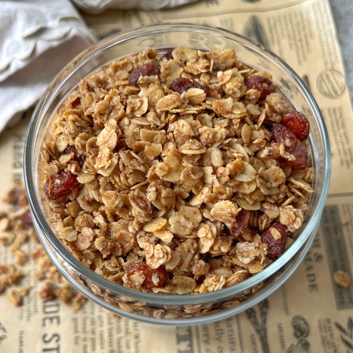 A glass bowl filled with cinnamon granola rests on a sheet of printed paper.