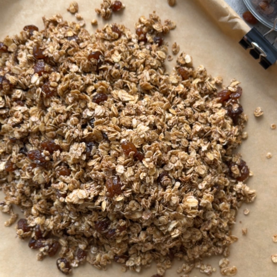 Loose Cinnamon Granola with oats and raisins spread on a sheet of parchment paper.