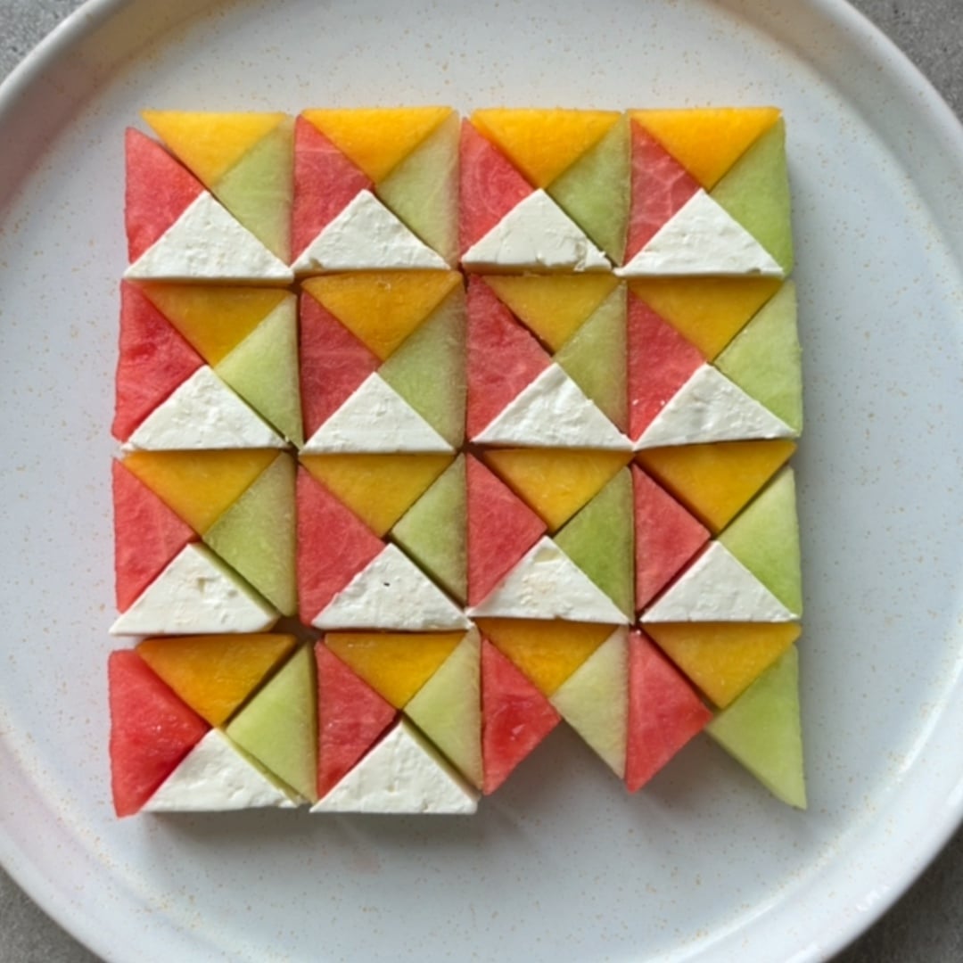 Two types of melon, nectarine, and feta triangles are arranged in a geometric pattern on a white ceramic platter.